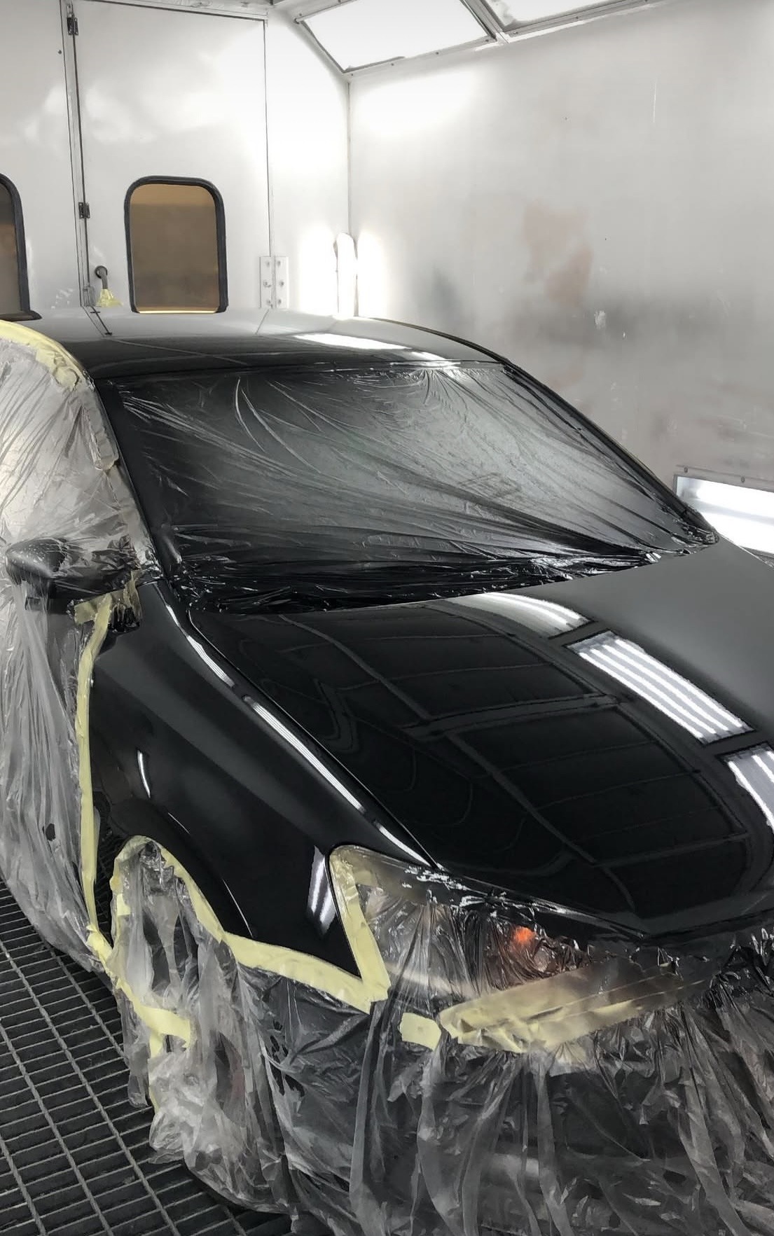 Zwarte auto, afgeplakt, in de spuitcabine